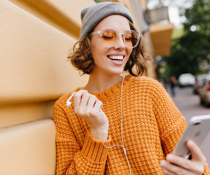 a girl on the street listening to online courses on her smartphone through headphones